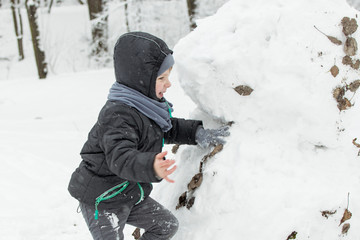 A little boy of 5-7 years old is playing outside in the snow in a park in winter.