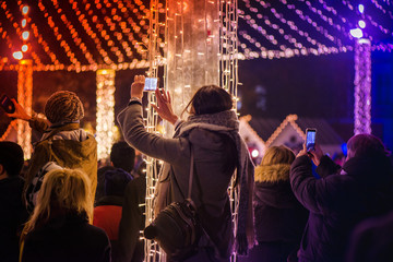 Christmas market and concert in city centre. People enjoying event, taking pictures and videos. Beautiful decorations and glowing lights.  