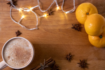 Fototapeta na wymiar Cup of coffee with orange mandarins and cinnamon sticks and anise stars sticks on the wooden table with garland