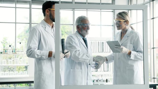 Group of chemists working in a lab. Young white male and female chemists with senior caucasian chemist working together in lab, writing on glass display. Science concept.