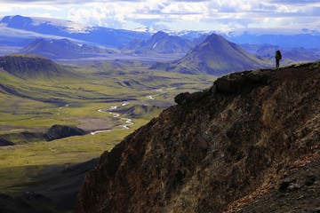 Naklejka premium Travel to Iceland (northern Europe). Walk through the Landmannalaugar nature reserve, mountains, plains and volcanoes. A tourist is at the top of a hill.
