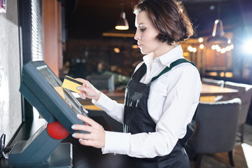 Serious concentrated young waitress with short hair standing at restaurant desktop computer and...