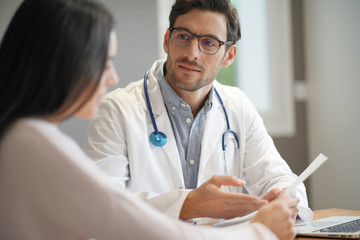  Modern young doctor speaking to patient in office
