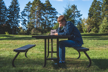 Fototapeta premium Concerned teenager sitting at a picnic table all alone with his phone.
