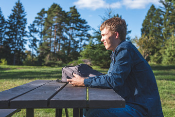 Fototapeta premium Concerned teenager sitting at a picnic table all alone with his phone.