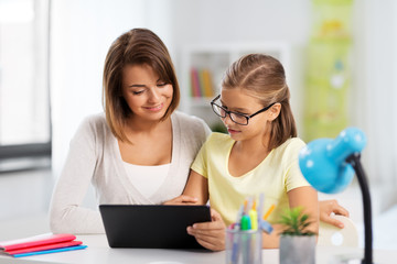 education, family and learning concept - mother and daughter with tablet pc computer doing homework...