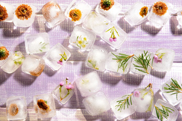 Beautiful flowers frozen in ice cubes on color wooden background