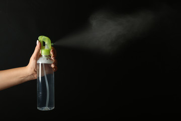 Woman spraying air freshener on dark background