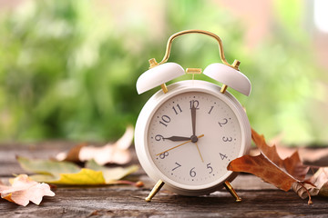 Alarm clock with autumn leaves on wooden table outdoors