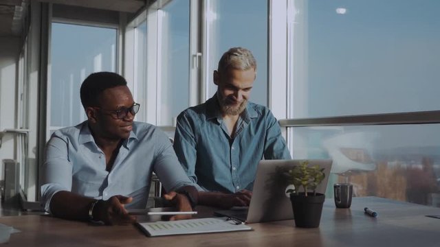 Two businessmen in casual are talking and using gadgets while working in the office. Business. Technology. Partnership.