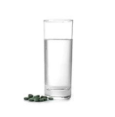 Glass of water with spirulina tablets on white background