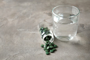 Glass of water with spirulina tablets on grey table