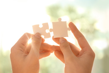 Woman with pieces of puzzle near window on sunny day, closeup