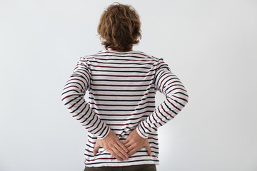 Young man suffering from back pain on light background