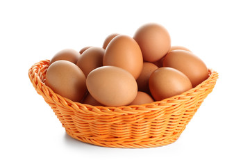 Wicker basket with raw brown chicken eggs on white background