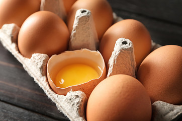 Cracked and whole chicken eggs in carton pack on dark wooden table, closeup