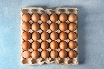 Carton pack with raw chicken eggs on color table