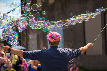 A freelance clown blowing hundreds of tiny, small and big bubbles at outdoor festival in city...