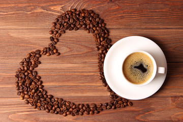  Cup of coffee and coffee beans posing in the shape of a heart on a wooden background top view. Flavored coffee