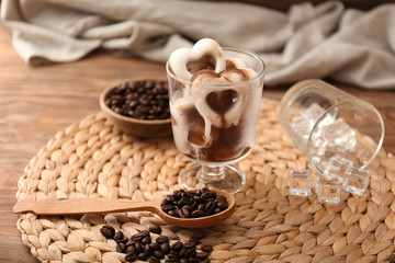 Glass with heart-shaped coffee ice pieces and beans on wicker mat