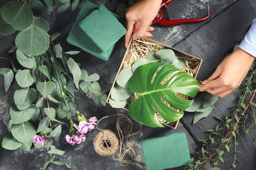 Florist preparing gift box with green branches on grey table