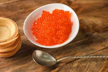 Plate with delicious red caviar on wooden table