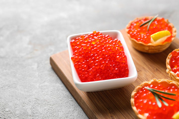 Bowl with delicious red caviar and canapes on wooden board, closeup