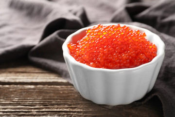 Bowl with delicious red caviar on wooden table