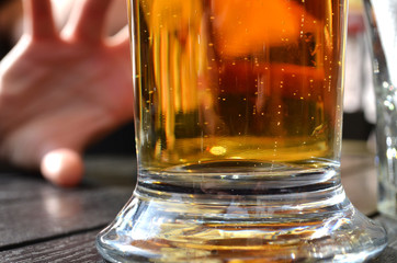 Close up of full glass of golden beer standing on wooden table in outdoor pub. Summer vacation begins. Concept of drinking problems and alcohol addiction  