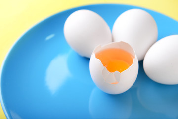 Plate with cracked and whole chicken eggs on color background, closeup