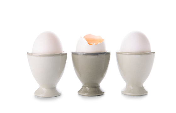 Holders with cracked and whole chicken eggs on white background