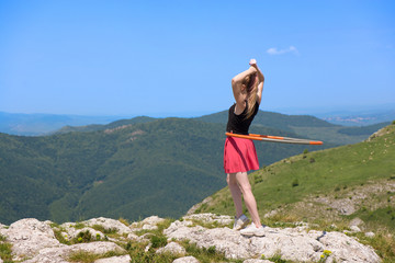 Young woman in pink skirts rotates hula hoop at the mountain top on beautiful nature background. Healthy lifestyle and love for fitness and sport. Freedom and fresh air outdoors  