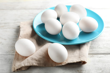 Plate with raw chicken eggs on light wooden table