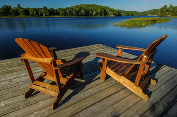 Fototapeta premium wooden Muskoka chairs on dock, overlooking deep blue lake