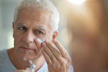 mature man in front of mirror using cosmetics