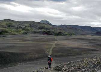 Experienced male hiker hiking alone into the wild with heavy backpack in black desert, Laugavegur hiking trail, Iceland