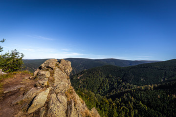 Fototapeta na wymiar Lookout Rysi skaly with Praded in the background, rocks in the foreground and green valley full of coniferous trees under. Jeseniky Czech Republic