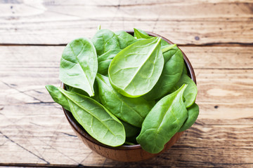 Fresh spinach leaves in bowl on rustic wooden table.