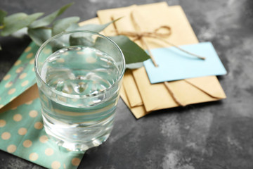 Glass of fresh water with envelops on grey table