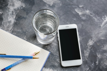 Glass of fresh water with mobile phone on grey table