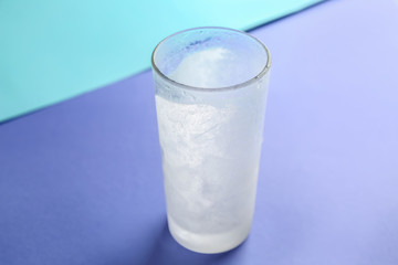 Glass of frozen water on color table