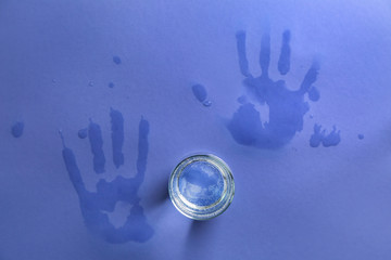 Glass of fresh water with wet palm prints on color table