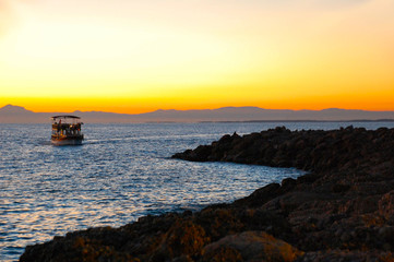 Obraz premium Boat trip on the Mediterranean Sea, the boat at sunset swims to the stone coast.