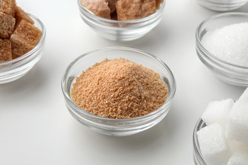 Bowls with different kinds of sugar on white background