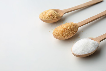 Different granulated sugar in wooden spoons on white background