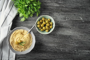Bowls with tasty hummus, olives and parsley on wooden table