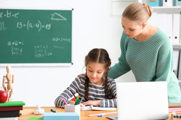 Cute girl with teacher doing homework in classroom