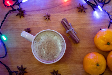 Cup of coffee orange mandarins, cinnamon sticks, anise stars  on the wooden background with garlands