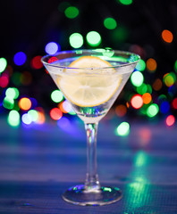 What to drink on christmas party. Cocktail glass with water and slice of lemon defocused garland lights. Detox drink to feel better. Hangover and detox. Detox after winter party. Health care concept
