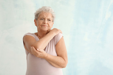 Senior woman suffering from pain in elbow on light background